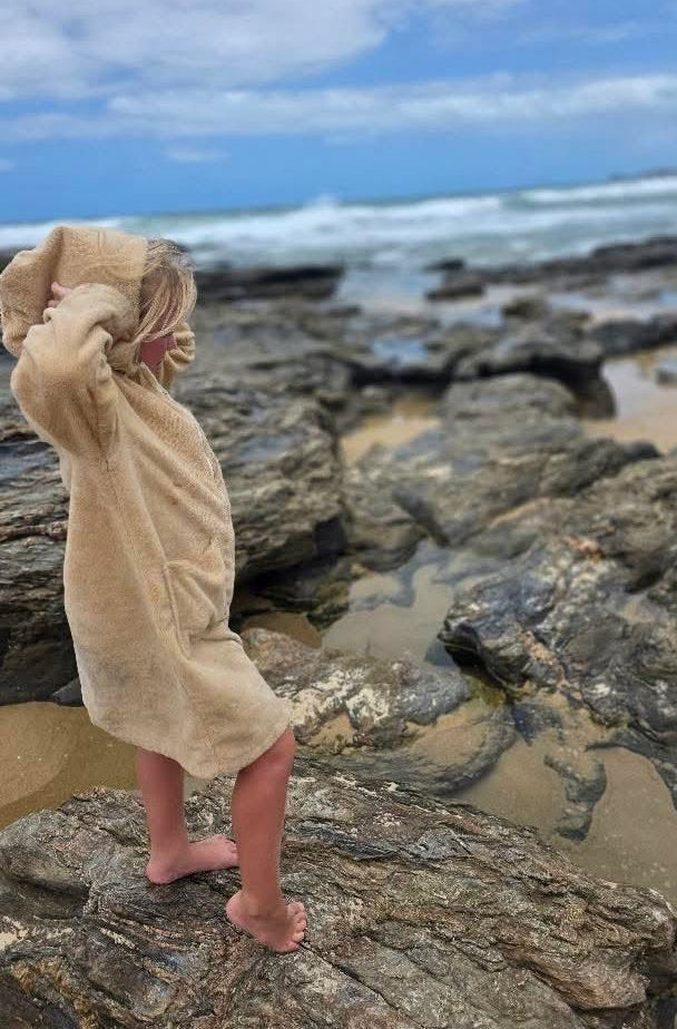 Person wrapped in a towel on a rocky beach with ocean and sky in the background